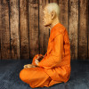 Vue latérale du moine en cire Luang Phor Sodh assis en méditation, robe bouddhiste orange