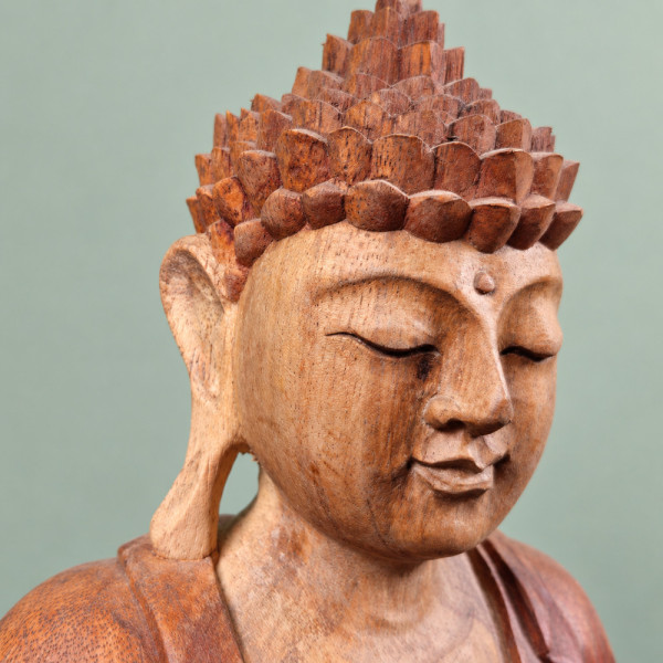 Gros plan de trois quarts sur le visage, l’oreille et la coiffure du Bouddha de l’accueil en bois de suar